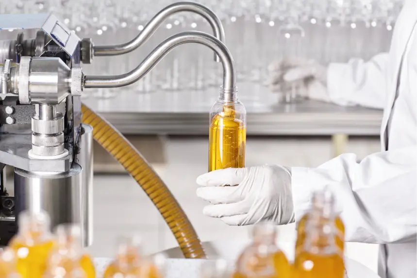 دستگاه نیمه‌اتوماتیک پرکن مایعات در حال پر کردن بطری‌های محصول در خط تولید.